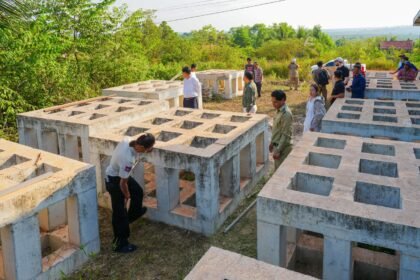 Large, square concrete artificial fish shelter frames being inspected by Cambodian officials and conservation experts in an outdoor field.